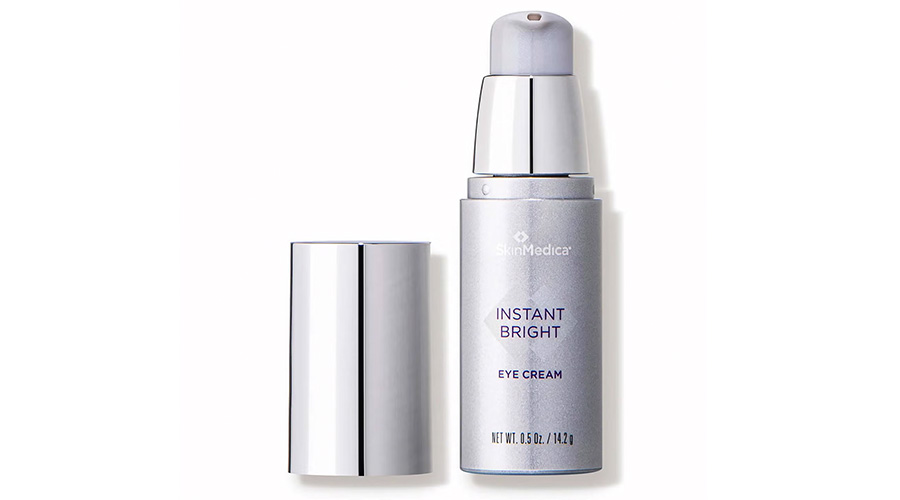 A silver bottle of SkinMedica Instant Bright Eye Cream with a pump dispenser, shown with its shiny silver cap removed and placed beside it, against a white background.