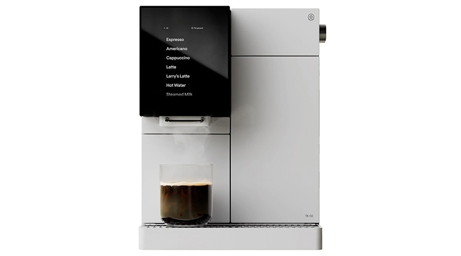 A modern white coffee machine with a black digital display screen showing drink options, brewing a cup of coffee, placed on a metal drip tray. Steam is visible rising from the glass cup below.