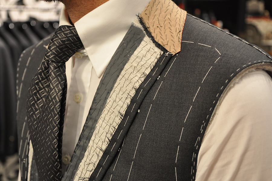 Close-up of a man wearing a partially tailored suit jacket, showing visible stitching, padding, and fabric layers on the shoulder and chest, over a white shirt and patterned tie.