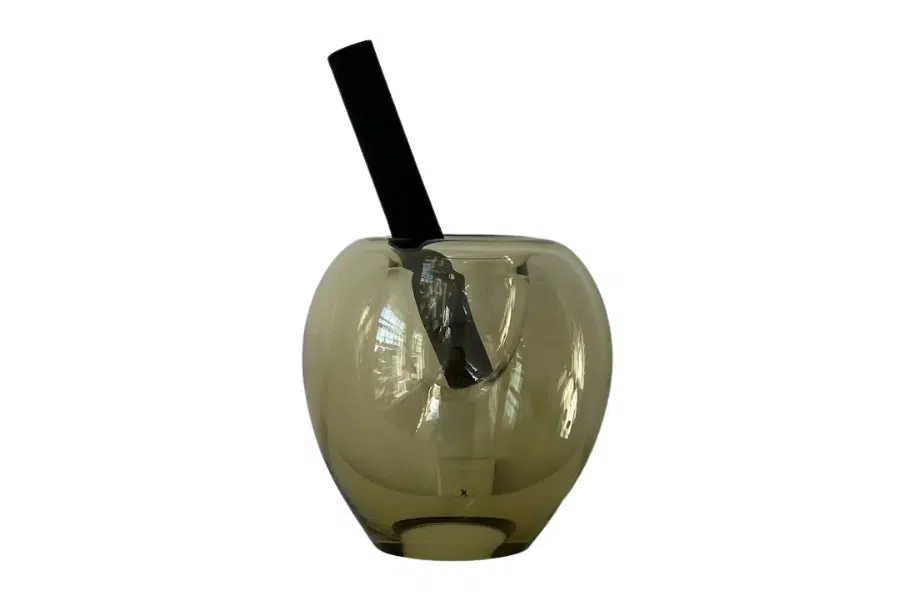 A translucent, smoky gray glass vase with a wide round body and a narrow opening, holding a single black rectangular object, possibly a stick or book, against a white background.