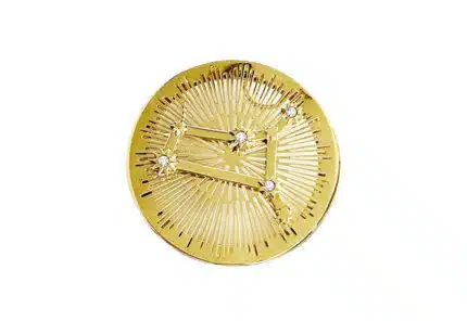A round gold pin featuring a constellation design with six small diamonds connected by engraved lines, set against a background of radiating linear patterns.