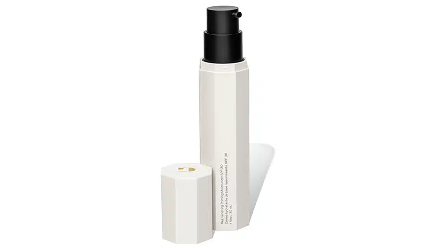A white, hexagonal bottle with a black pump dispenser and a matching white cap placed beside it. The bottle has vertical text and is photographed against a white background.
