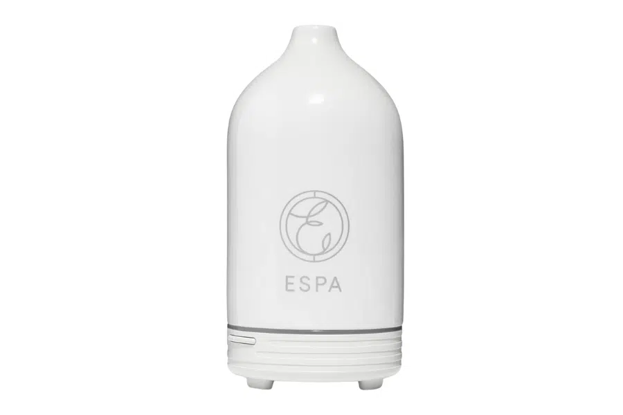 A white ceramic ESPA essential oil diffuser with a simple, rounded design, a small spout at the top, and the ESPA logo on the front. The base has subtle horizontal grooves and a small button.