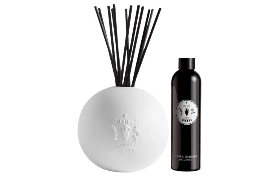 A white spherical diffuser with black reeds next to a tall, black fragrance refill bottle, both featuring embossed or printed decorative logos, set against a white background.