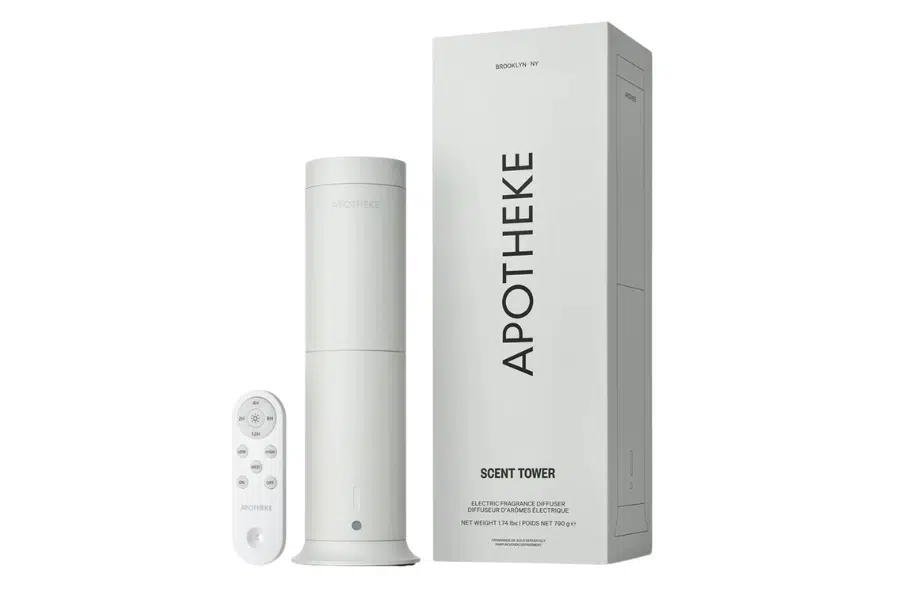 A white rectangular box labeled APOTHEKE SCENT TOWER stands beside a sleek, cylindrical device and a matching white remote control with labeled buttons, all set against a plain white background.