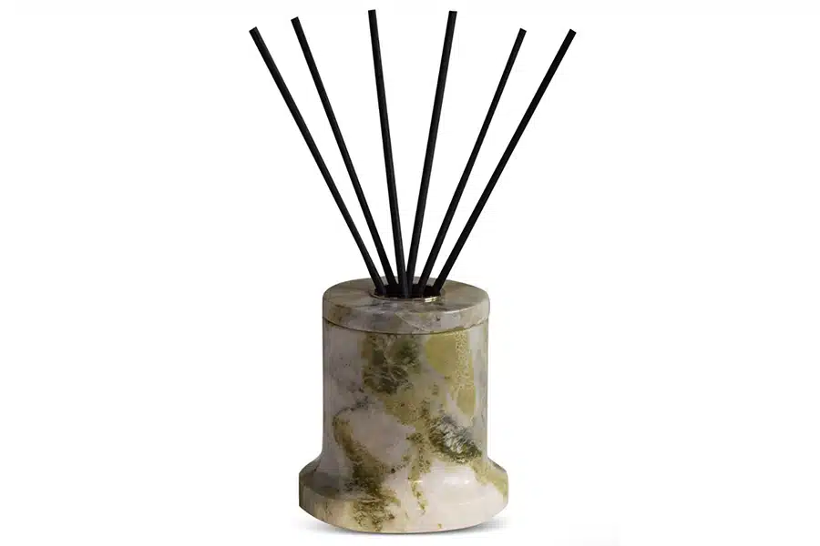 A marble-patterned reed diffuser with a cylindrical base holds several black diffuser sticks fanned out at the top.
