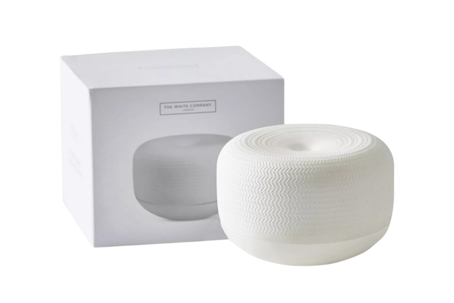 A white ceramic diffuser with a textured circular pattern is placed in front of its matching box, which displays a photo and branding from The White Company. Both are set against a plain white background.