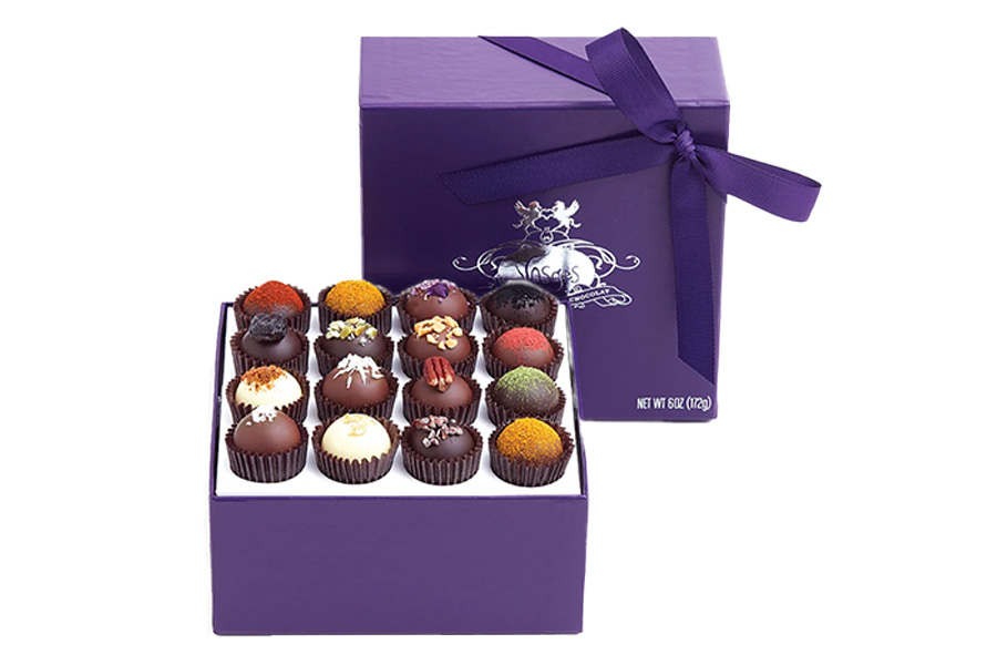 A purple gift box with a matching ribbon, open to display an assortment of colorful gourmet chocolates arranged neatly in rows inside.