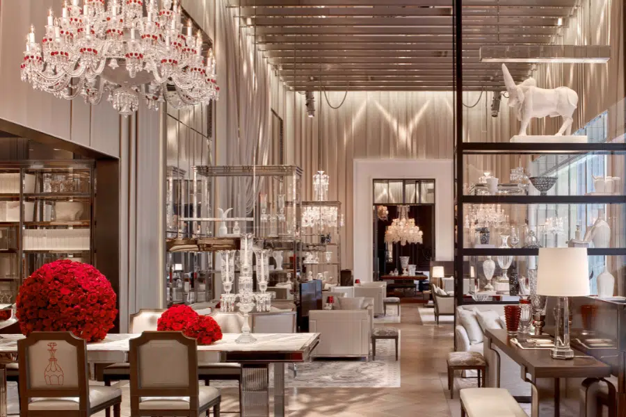 Elegant, modern dining room with crystal chandeliers, white furniture, glass display cases, and large red rose arrangements. A white unicorn sculpture decorates the space, creating a luxurious, sophisticated atmosphere.