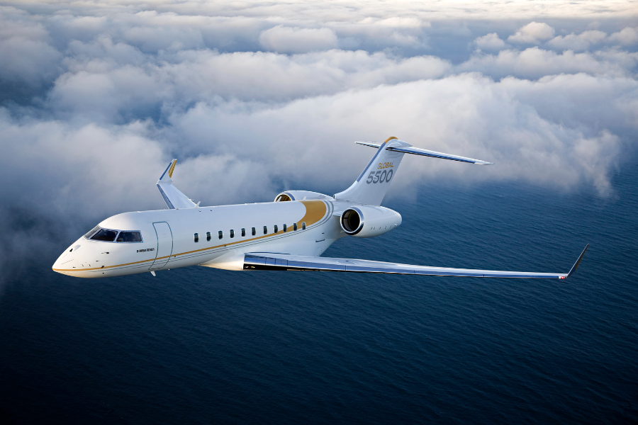 A white and gold private jet flies above the clouds over the ocean, with its wings tilted slightly upward and the words Global 5500 visible on the tail.