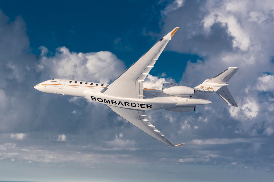 A white Bombardier Global 7500 business jet with BOMBARDIER written on its fuselage is flying through the sky against a backdrop of clouds, with its wings tilted upward in a dynamic angle.