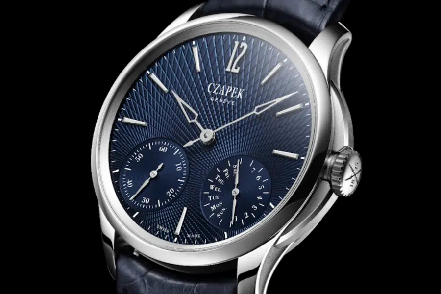 A luxury Czapek Genève wristwatch with a textured blue dial, silver hands, three subdials, silver hour markers, and a date display, set in a polished stainless steel case with a dark leather strap.