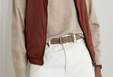A person wearing a beige long-sleeve shirt, a rust-colored zip vest, white pants, and a tan belt with a silver buckle. The image focuses on the torso and waist, showing the clothing details.