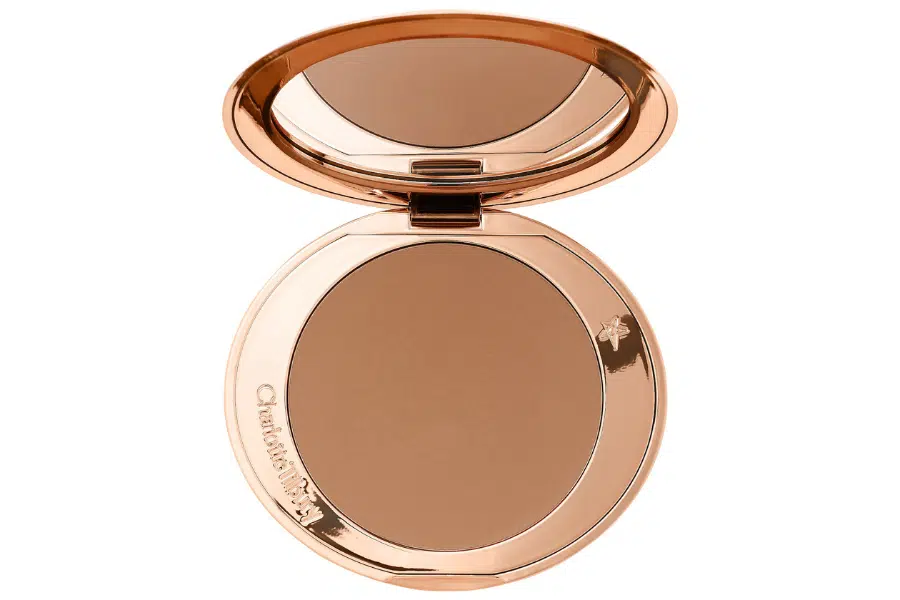 An open compact with a bronze powder and a built-in mirror, housed in a shiny rose gold case. The powder is smooth and unused, with Charlotte Tilbury engraved on the edge.