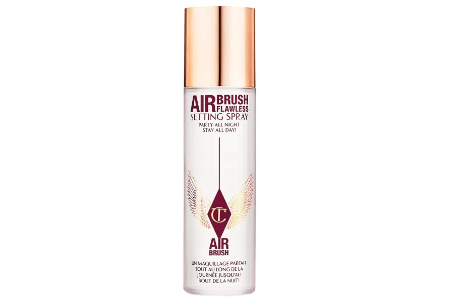 A bottle of Charlotte Tilbury Airbrush Flawless Setting Spray with a rose gold cap, clear body, and maroon and gold lettering, featuring a winged logo in the center.