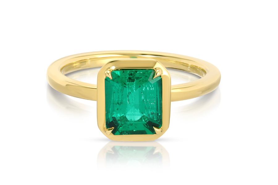 A gold ring featuring a rectangular, emerald-cut green gemstone set in a simple bezel setting, displayed on a white background.