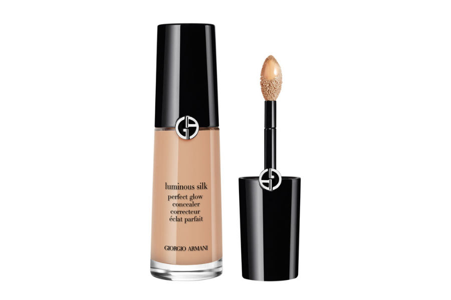 A bottle of Giorgio Armani Luminous Silk Concealer with a black cap, shown next to its applicator wand with a sponge tip, both featuring the brand’s silver GA logo.