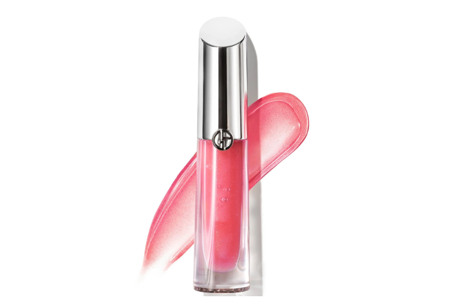 A tube of pink lip gloss with a silver cap stands in front of a pink gloss smear on a white background.