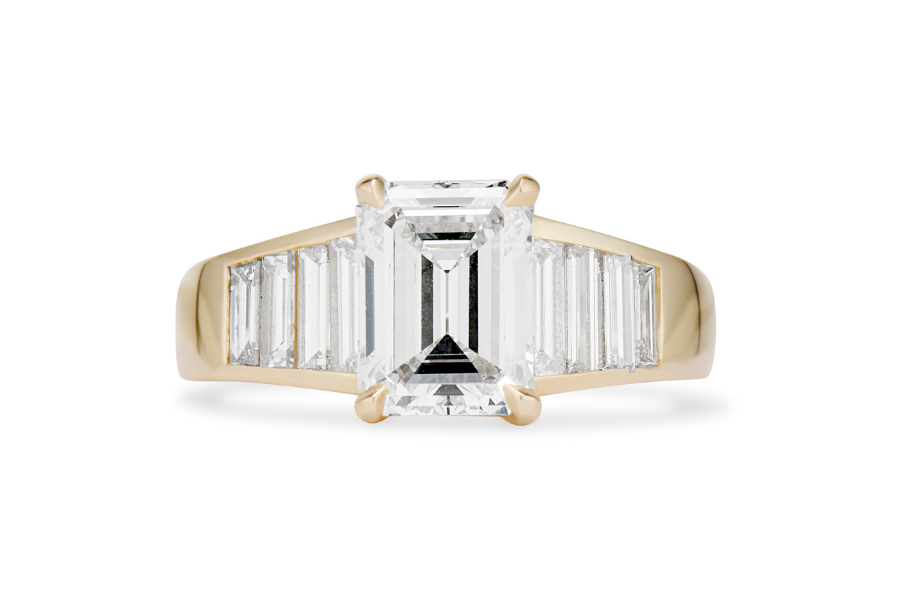 A gold ring with a large emerald-cut diamond center stone, flanked by tapered baguette diamonds set into the band on each side.