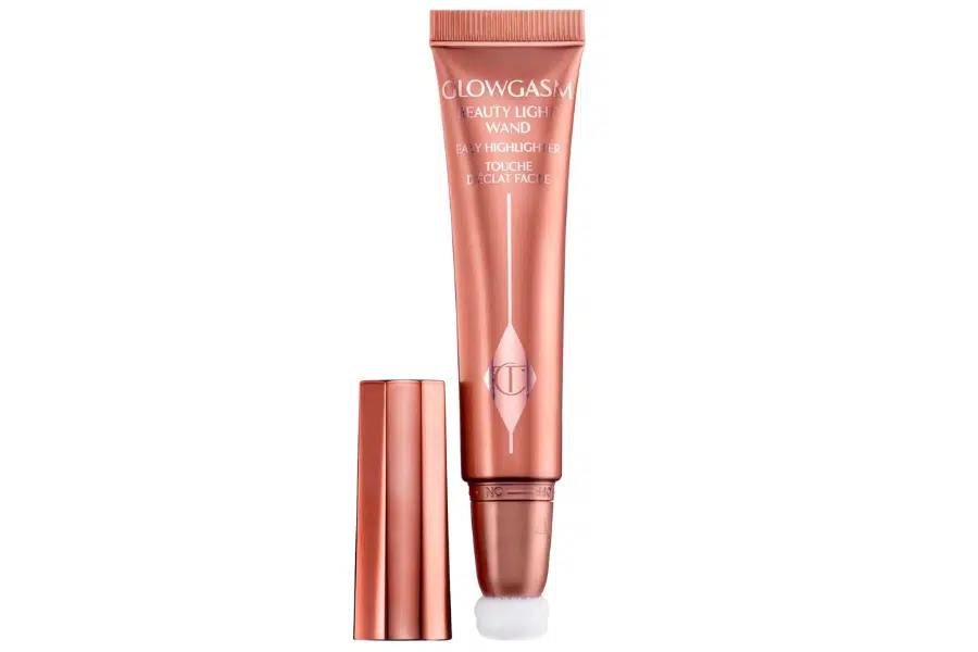 A rose gold tube of Charlotte Tilbury Beauty Light Wand highlighter with its cap off, revealing a soft cushion applicator tip, displayed against a white background.