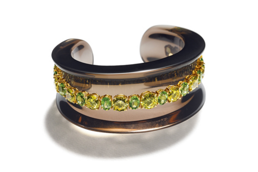 A wide, glossy brown cuff bracelet featuring a central row of round green and yellow gemstones set in gold. The bracelet is displayed on a white background.