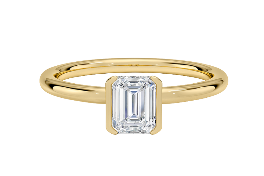 A gold ring with a thin band featuring an emerald-cut, clear diamond set in a simple, bezel-style setting at the center.