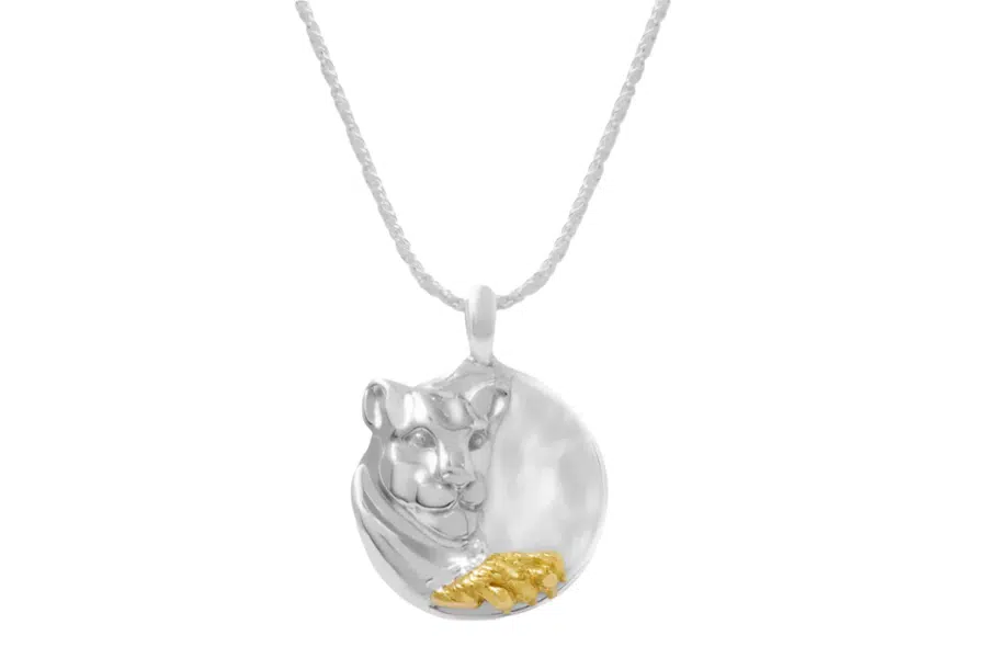 A silver necklace with a round pendant featuring a sculpted animal head, possibly a big cat, and a small gold-toned detail shaped like a paw at the bottom.