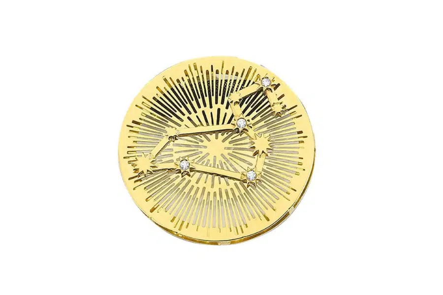 A round gold compact with engraved radiating lines and a constellation design, accented by several small sparkling gems.