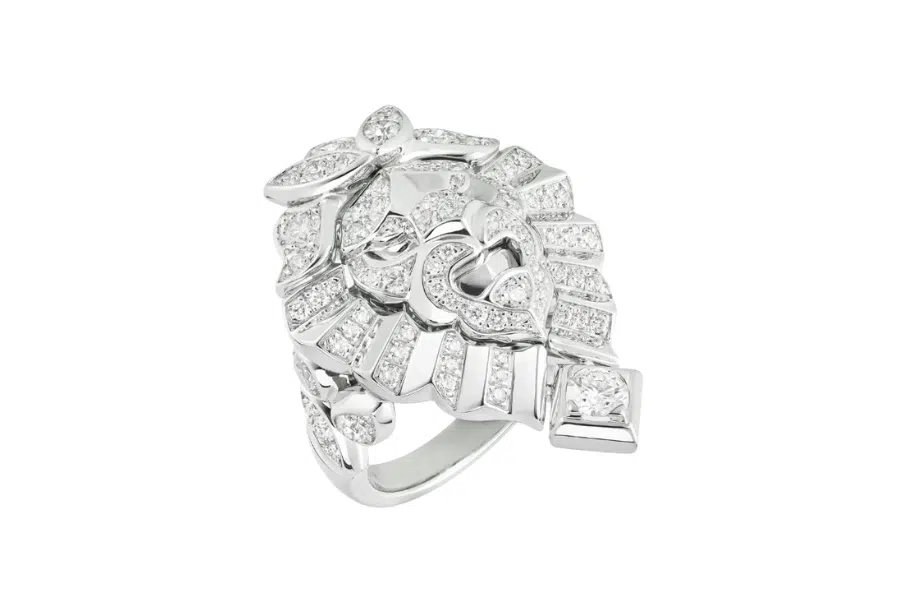 A silver ring with an intricate, floral-inspired design, encrusted with numerous small white diamonds and a prominent square-cut diamond on one side, displayed on a white background.