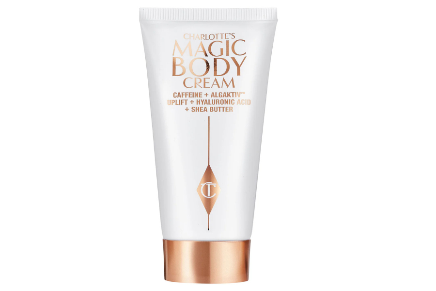A white tube of Charlotte’s Magic Body Cream with rose gold accents, featuring text highlighting ingredients like caffeine, Algaktiv, hyaluronic acid, and shea butter.
