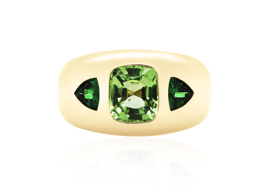 A gold ring with a large rectangular green gemstone in the center, flanked by two smaller triangular green stones, set against a white background.