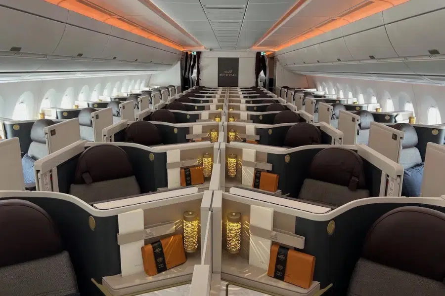Etihad Airways business class cabin featuring spacious, luxurious seats arranged in a staggered layout with privacy dividers, mood lighting, and amenities placed on each seat.