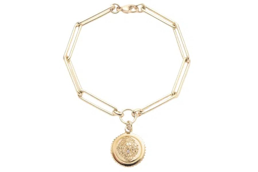 A gold chain bracelet with elongated links and a round, textured locket charm featuring a cluster of small, sparkling stones in the center.
