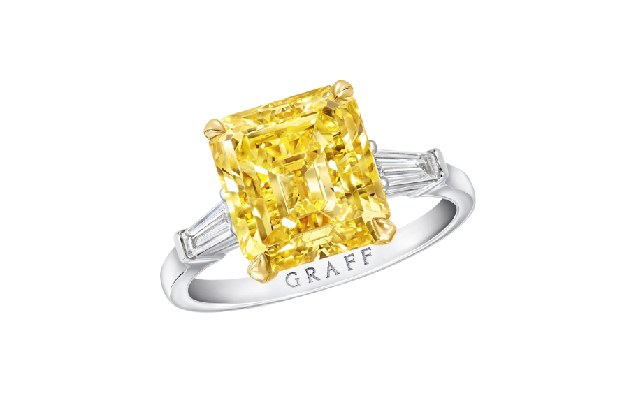A platinum ring with a large, rectangular yellow diamond in the center, flanked by two tapered baguette white diamonds, and “GRAFF” engraved on the band.