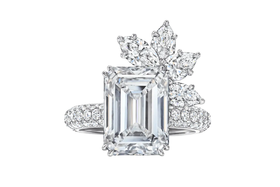 A silver ring featuring a large emerald-cut diamond at the center, complemented by a cluster of marquise-cut diamonds arranged in a floral pattern on one side and a band encrusted with smaller diamonds.