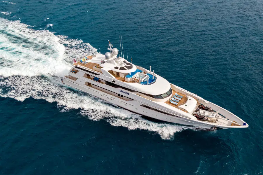 A large white luxury yacht cruises through deep blue ocean water, creating a trail of white waves behind it under a clear sky.