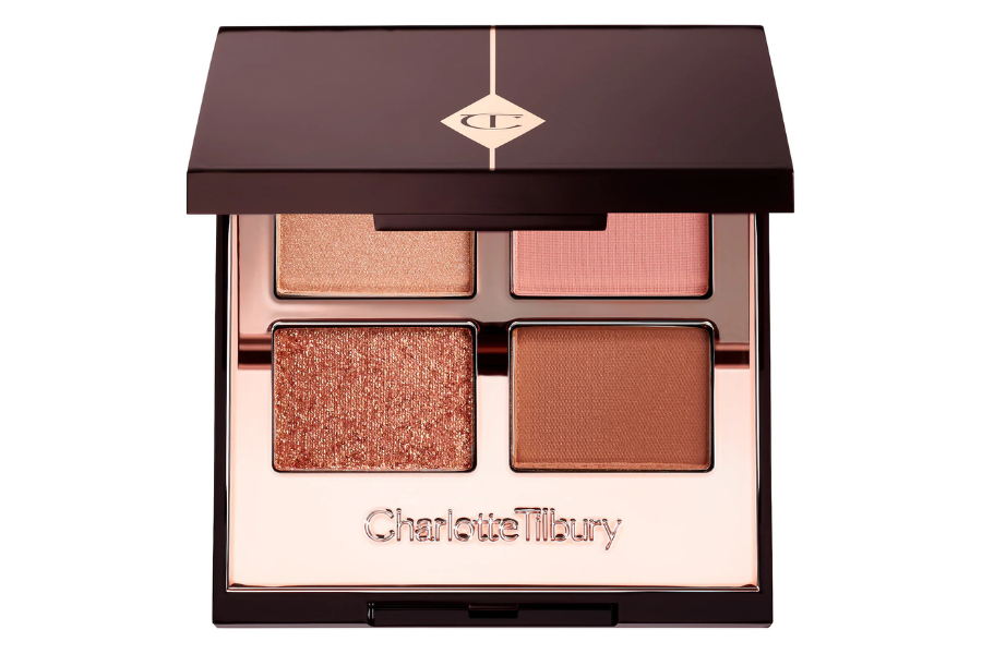 An open Charlotte Tilbury eyeshadow palette with four shades: a shimmery peach, a matte pink, a glittery bronze, and a matte brown, in a dark brown compact with a mirror.