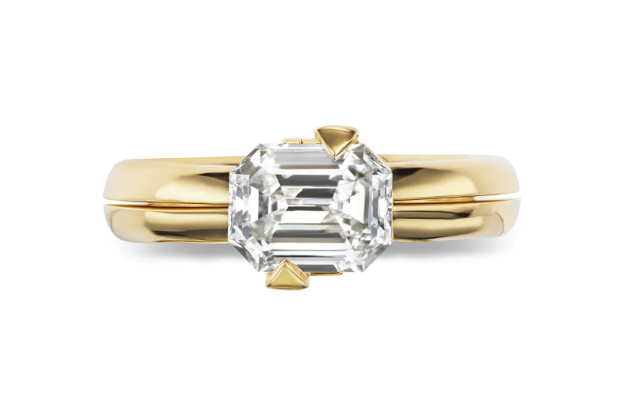 A gold ring featuring a large, emerald-cut clear diamond set in a simple prong setting, displayed against a white background.