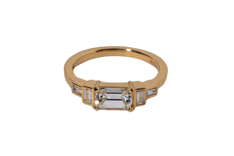 A gold ring featuring a rectangular emerald-cut central diamond flanked by two smaller baguette-cut diamonds on each side, all set in a sleek, modern band.