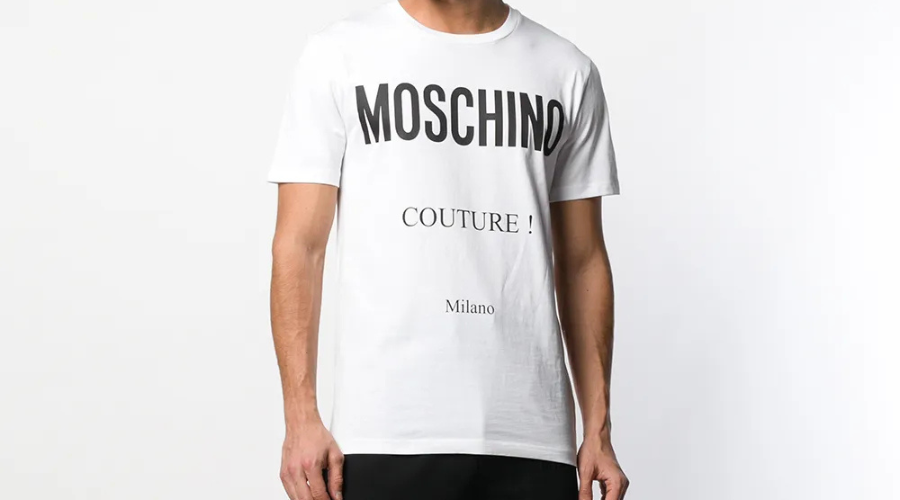 A person wearing a white T-shirt with the words MOSCHINO COUTURE! Milano printed in bold black letters on the front, standing against a plain white background.