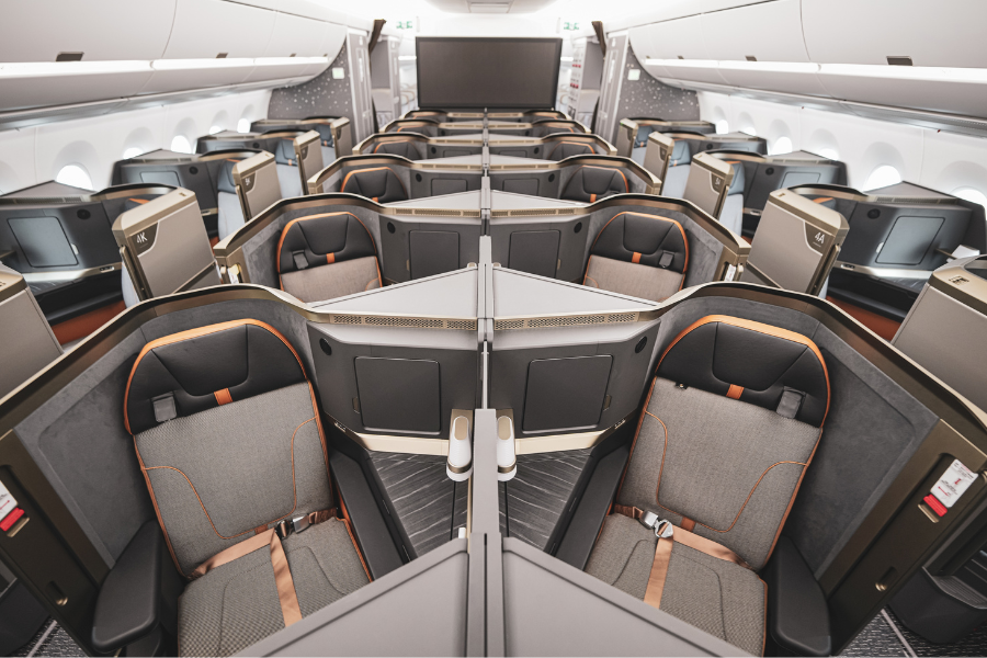 Business class cabin on a modern airplane featuring spacious, individual suites with grey seats, orange trim, and privacy partitions, arranged in a staggered layout for comfort and privacy.