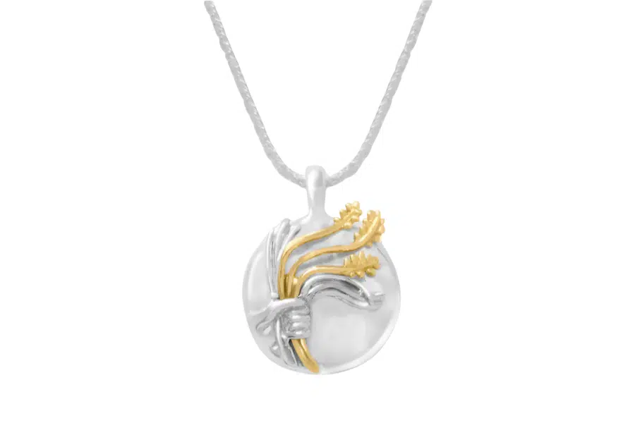 A round silver pendant on a chain featuring a raised design of a hand holding three golden wheat stalks. The pendant has both silver and gold tones, creating a two-tone effect.