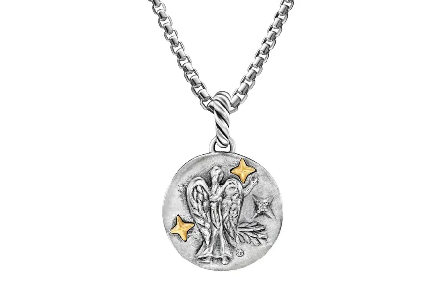 A silver chain necklace with a round pendant featuring an engraved angel, two small gold star accents, and a leaf design.