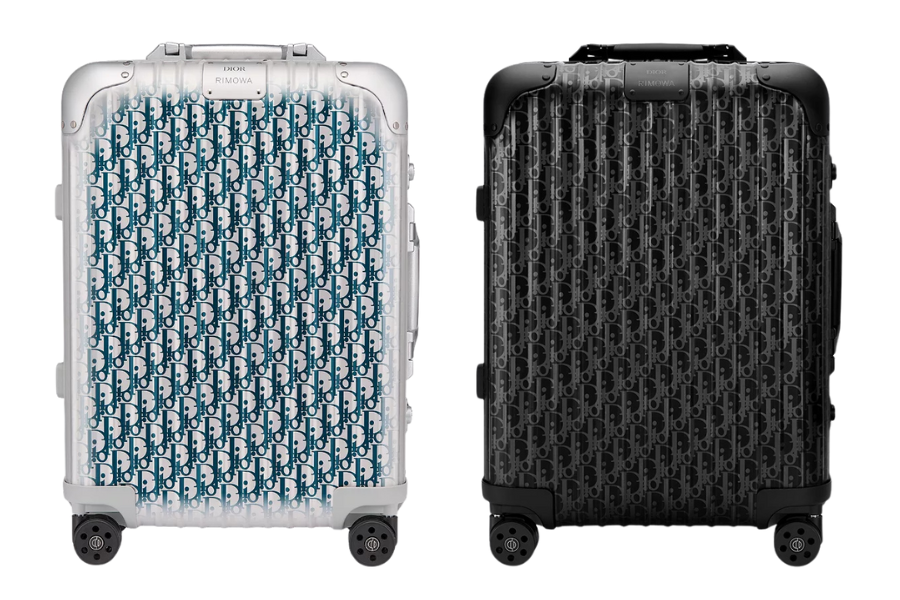 Two designer carry-on suitcases side by side: one silver with a blue Dior monogram pattern, the other black with a textured Dior monogram pattern. Both have four wheels and rounded corners.