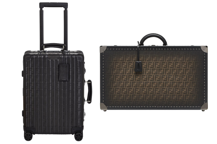 Two luxury suitcases: one is a black, hard-shell rolling suitcase with an extended handle; the other is a brown, rectangular suitcase with a monogram pattern and black leather handle.