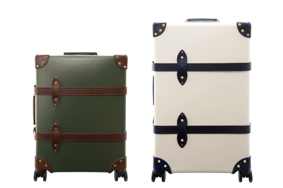 Two vintage-style suitcases with leather straps and corner protectors: one is dark green with brown accents, and the other is off-white with navy blue accents. Both have wheels and are standing upright.