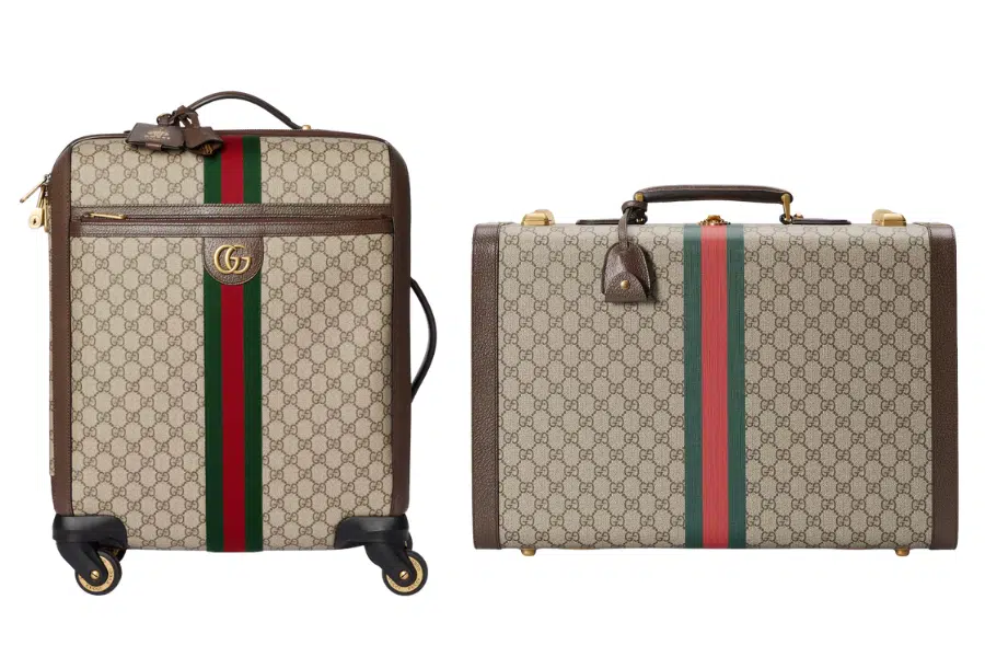 Two Gucci suitcases with beige monogram canvas, brown leather trim, red and green stripes, and gold hardware; one is a wheeled carry-on, the other is a structured briefcase with a top handle.