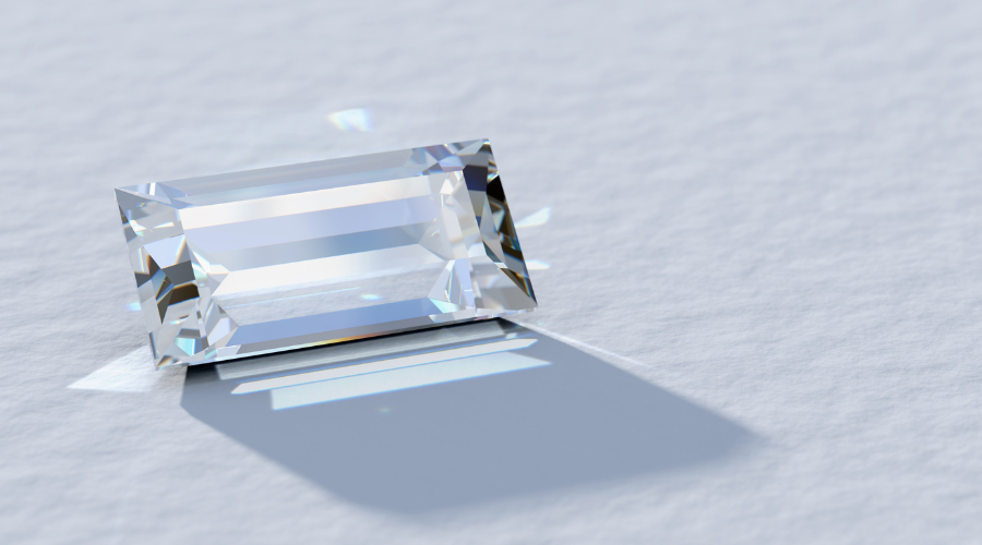 A rectangular, faceted clear gemstone rests on a textured white surface, casting a distinct shadow and reflecting light in subtle rainbow hues.