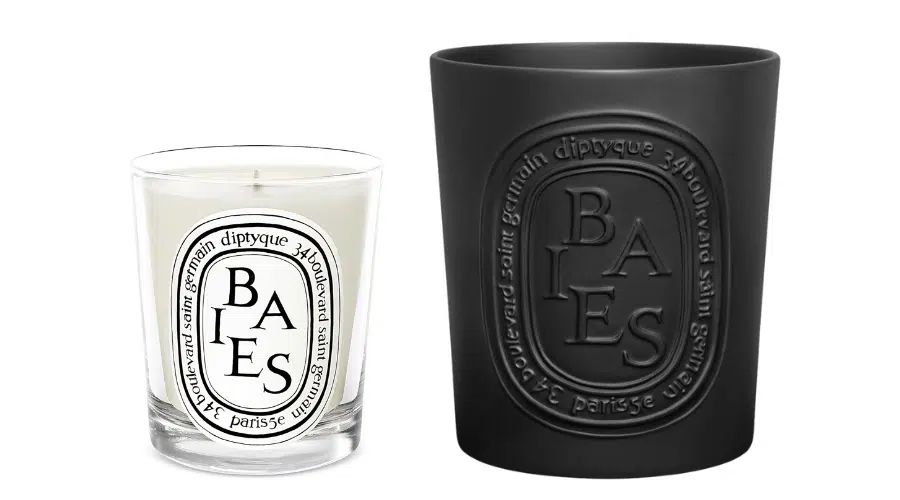 A clear glass Diptyque Baies candle with a white label next to a larger black glass Diptyque Baies candle with an embossed label. Both show the brand’s oval logo and text.