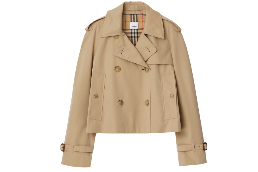 A cropped, double-breasted beige trench coat with button details, belted cuffs, and a plaid lining on the inside collar.